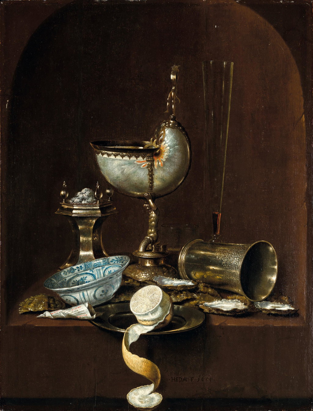 Still life with a silver-gilt-mounted nautilus cup, a beaker on its side, a peeled lemon on a plate, oyster shells, a blue and white porcelain bowl, a silver salt cellar and other objects on a stone ledge, in an arched niche. Image courtesy of Christie's